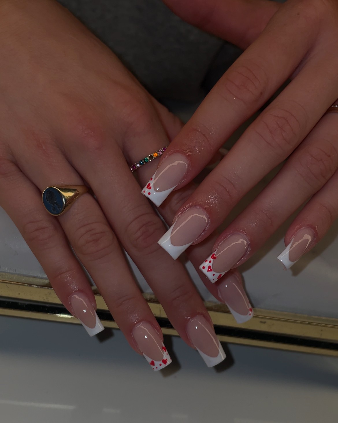Twee handen met lange French nagels met kleine rode hartjes en een gouden zegelring