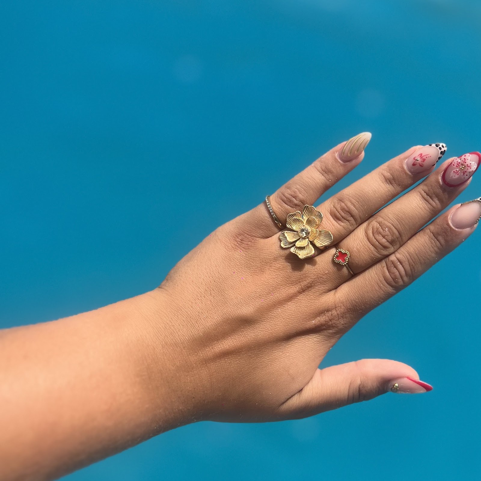 Hand met versierde nagels en een gouden bloemring boven blauw water