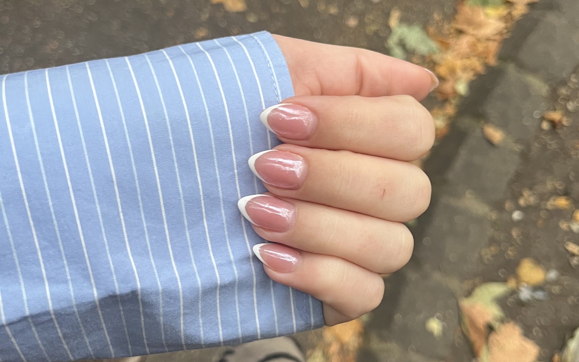 Hand met naturel French nagels uit een blauw gestreepte mouw